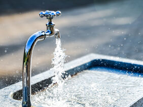 Aus einem silbernen Wasserhahn läuft Wasser in ein Becken.